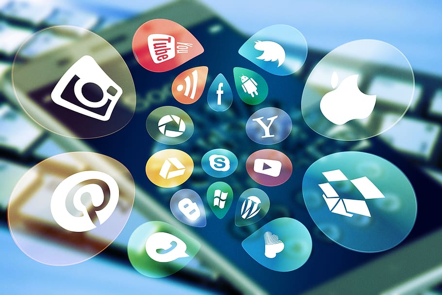 Icons of various social media platforms on an out-of-focus background with a cell phone and keyboard.
